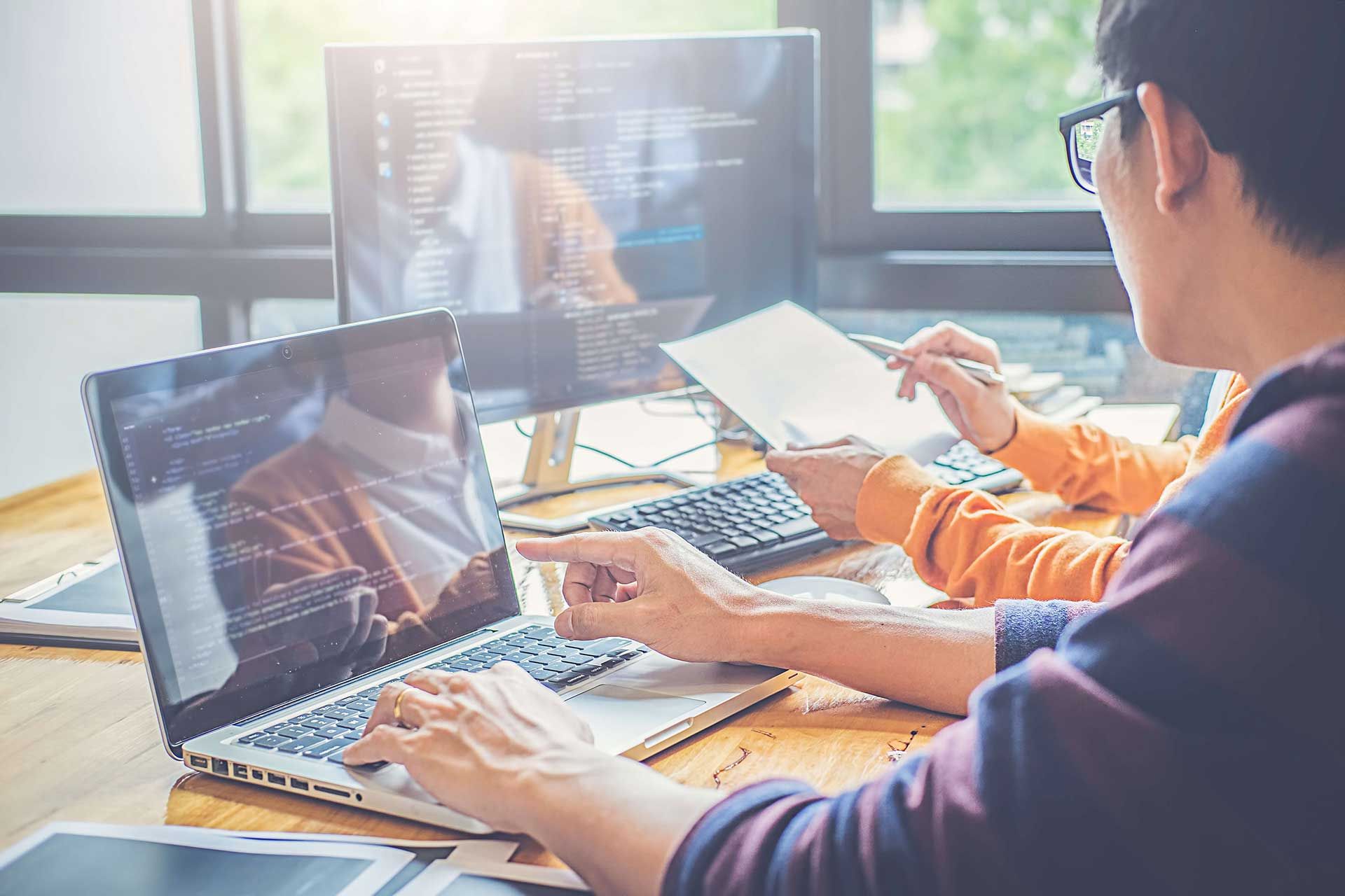 Man working on his laptop with a co-worker at a desk. 
